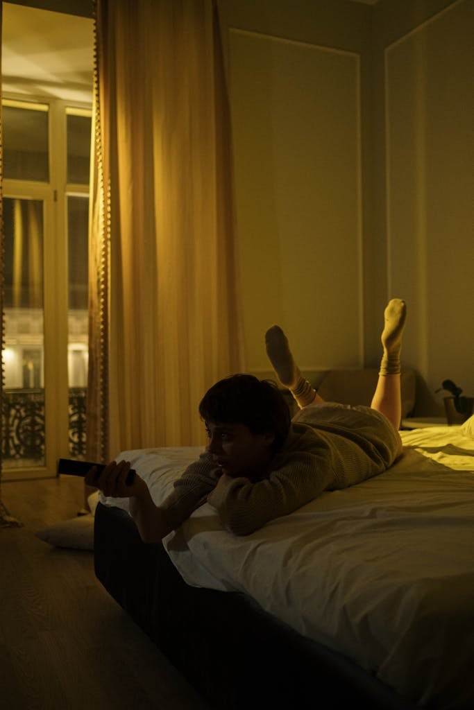 Photo of a Woman Lying on Her Bed while Using a Remote Control