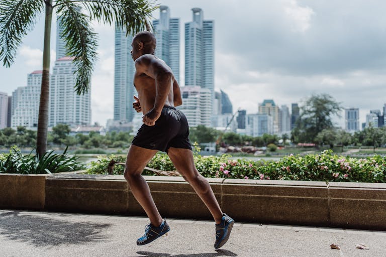 Shirtless Man in Black Shorts Running on Concrete Sidewalk