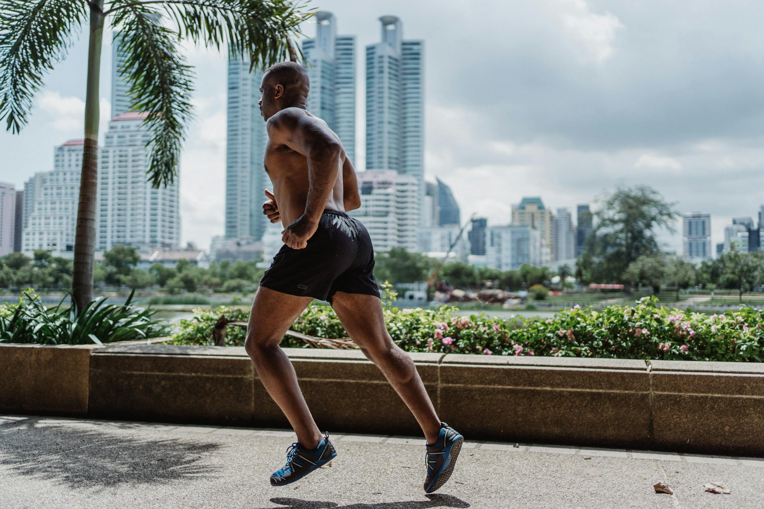 Shirtless Man in Black Shorts Running on Concrete Sidewalk