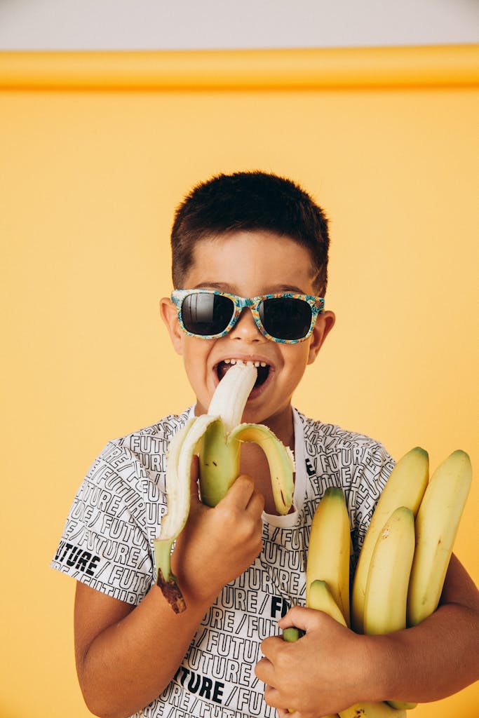 Boy in Sunglasses Eating a Banana and Holding a Bunch of Bananas