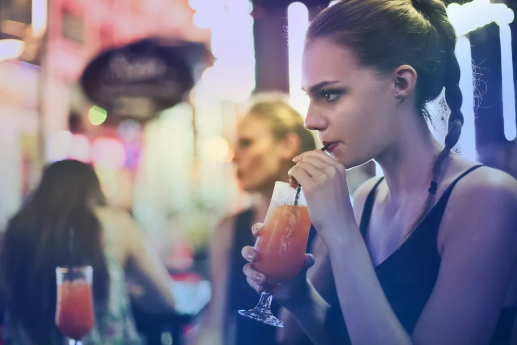 A young woman sipping a cocktail in a vibrant nightlife setting with friends. - testosterone