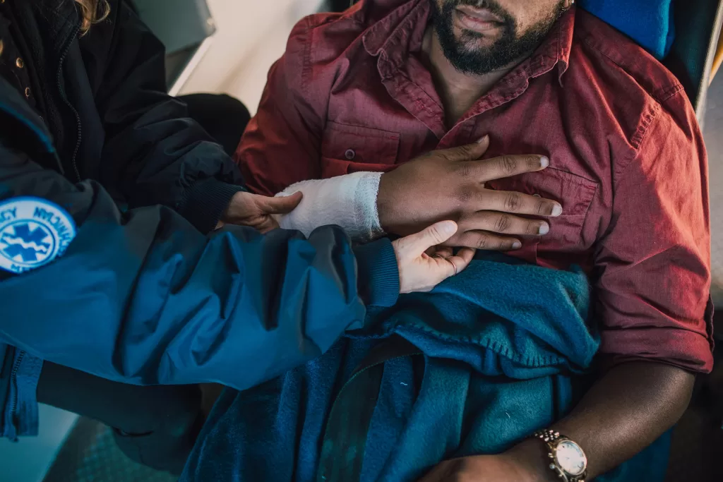 Paramedic assisting injured patient with arm bandaged in an emergency scenario.